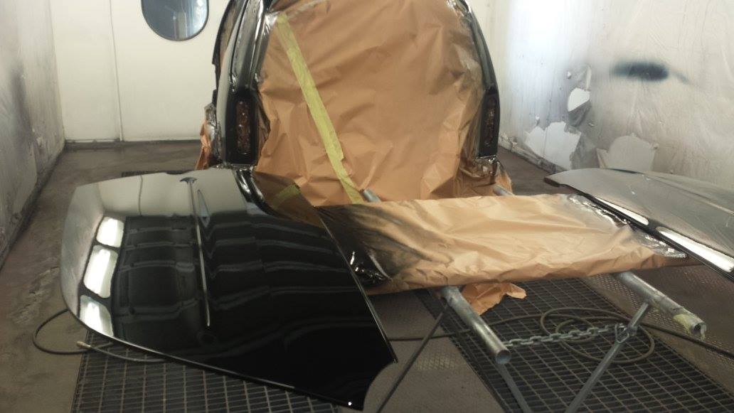 Parti di auto nere in una cabina di verniciatura, alcune ricoperte di carta marrone chiaro, un lavoro in corso.