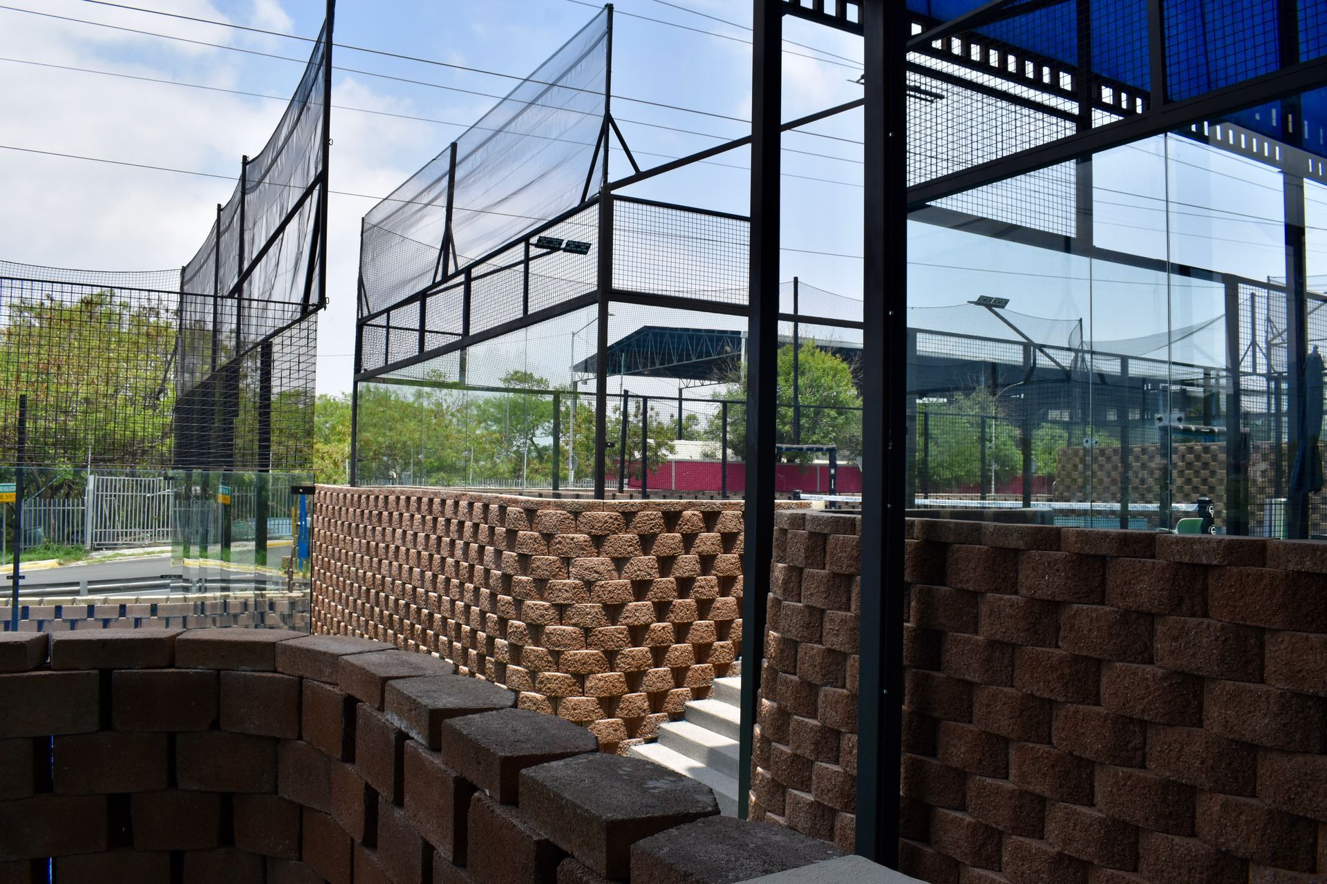 Pista deportiva al aire libre con valla de red y muros de ladrillo apilado en construcción.