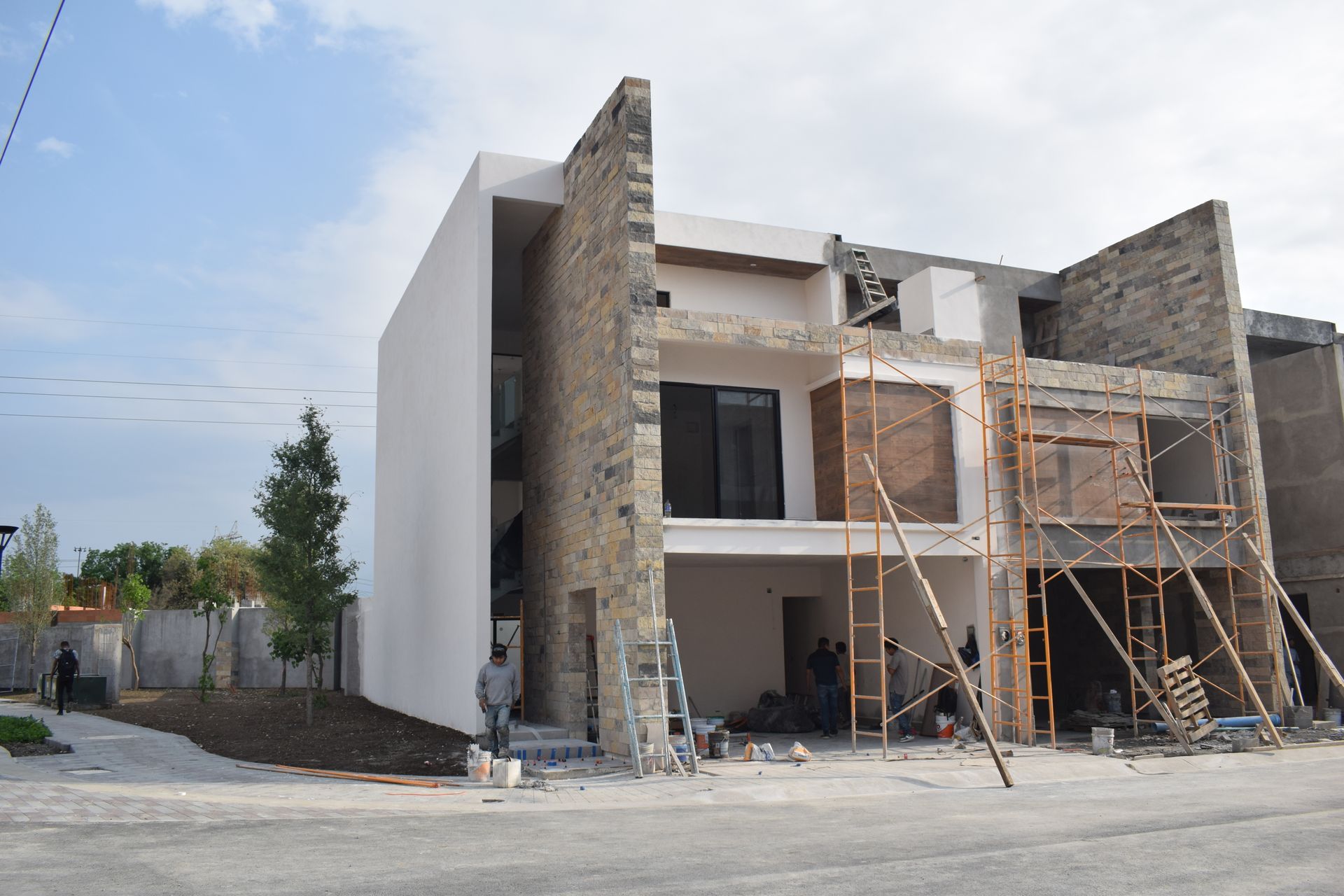 Casa parcialmente construida con fachada de piedra, andamios y trabajadores en una obra.