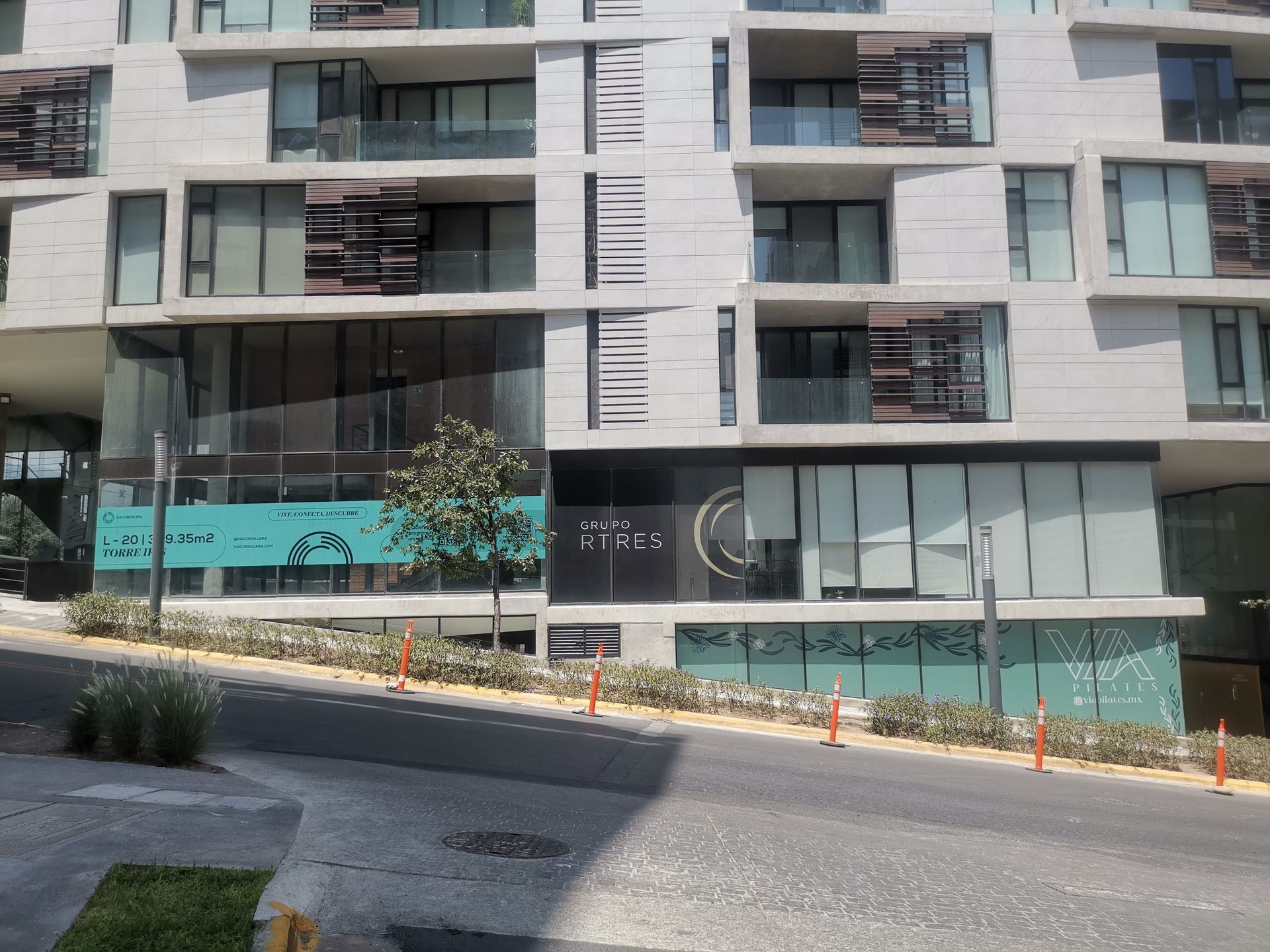 Edificio de apartamentos moderno con balcones y escaparates acristalados junto a una calle pavimentada en construcción.