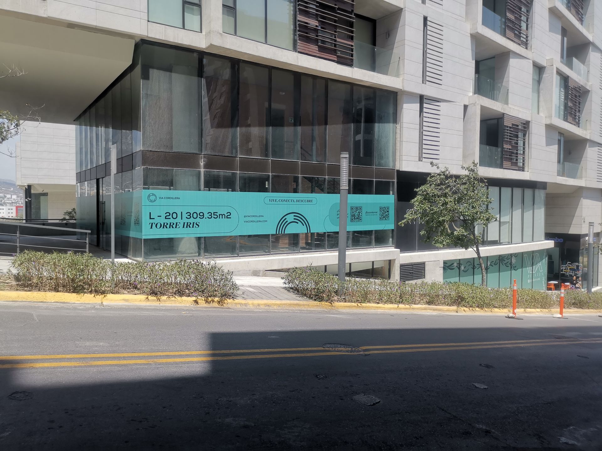 Edificio de apartamentos moderno con balcones, cartel de construcción turquesa y una calle enfrente.