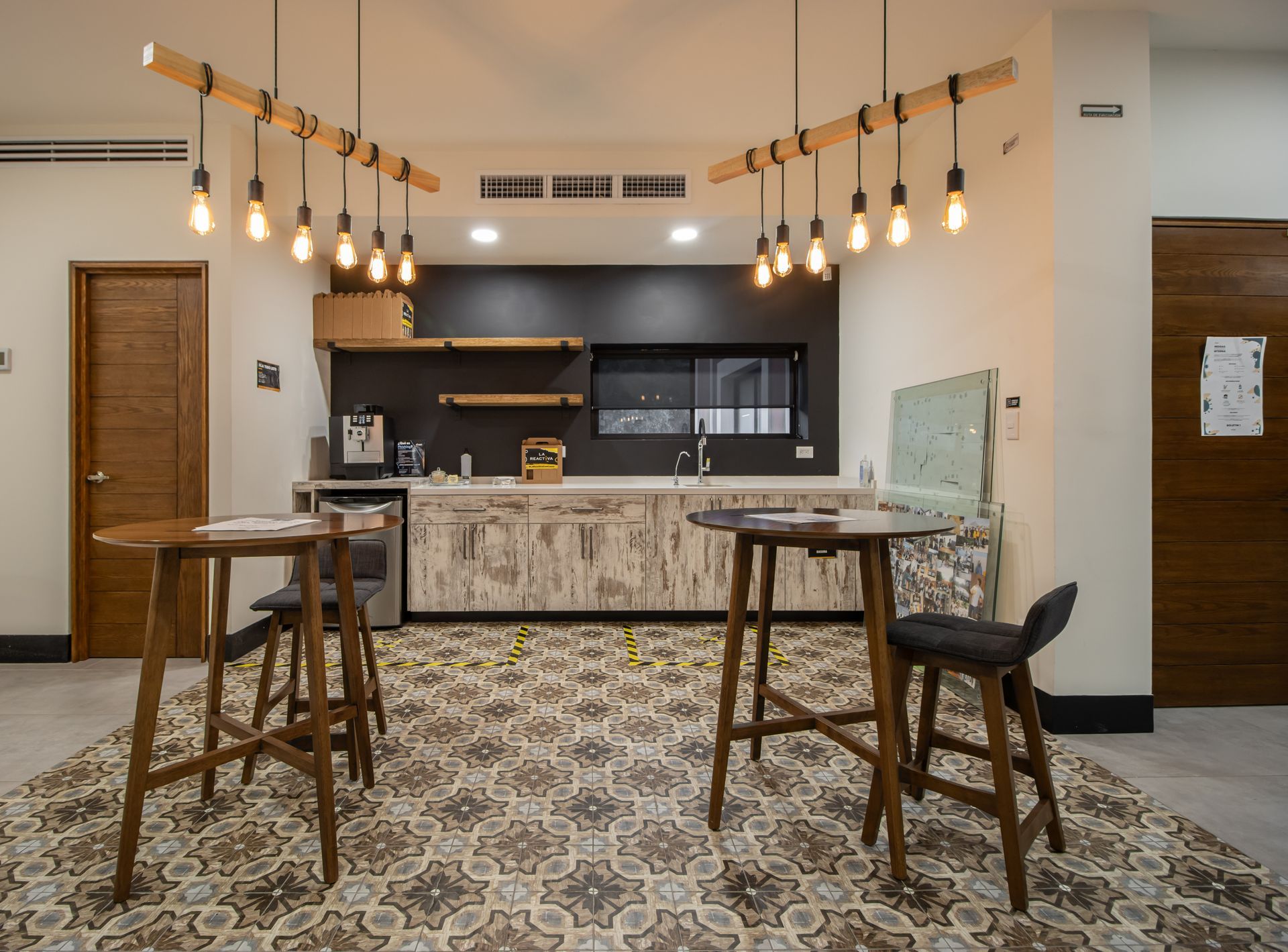 Cocina y zona de bar modernas con suelo estampado, lámparas colgantes y dos mesas altas con taburetes.