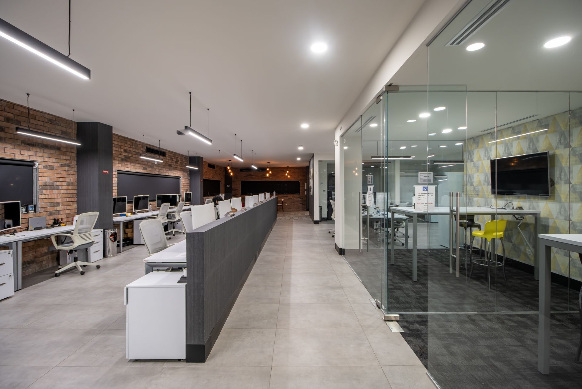 Oficina moderna de planta abierta con escritorios, salas de reuniones acristaladas y un largo pasillo central bajo.