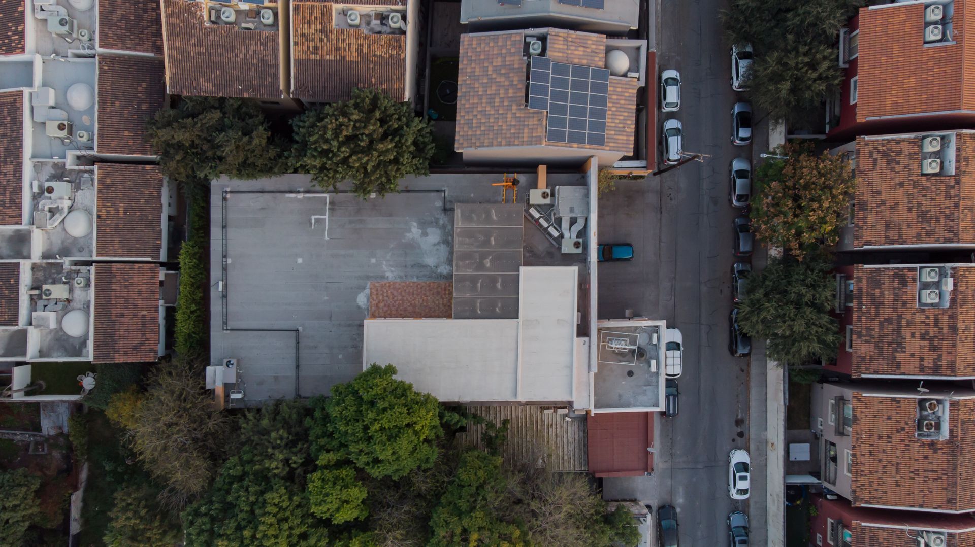 Vista aérea de un patio residencial y tejados junto a una calle estrecha, con árboles y coches aparcados.