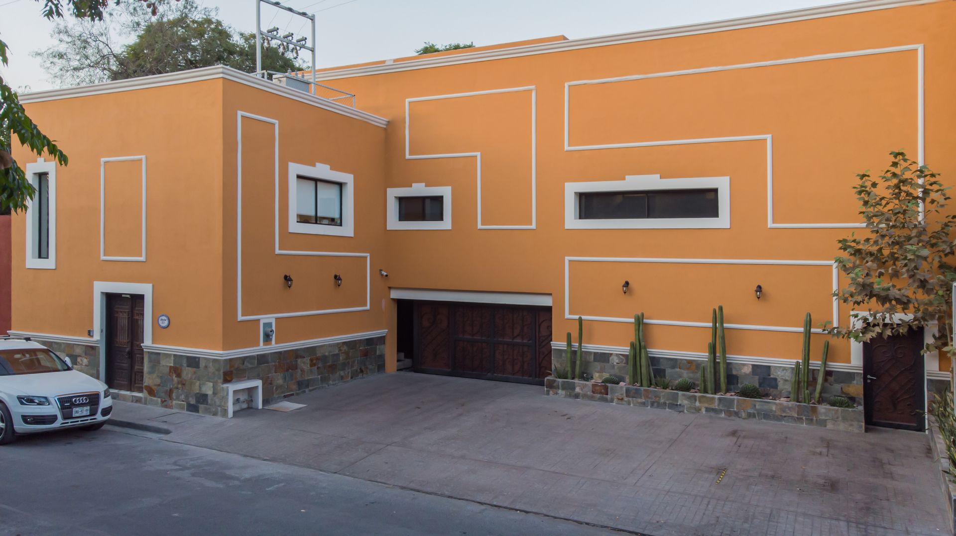 Fachada de casa moderna de color naranja con molduras geométricas blancas y garaje en una calle tranquila.