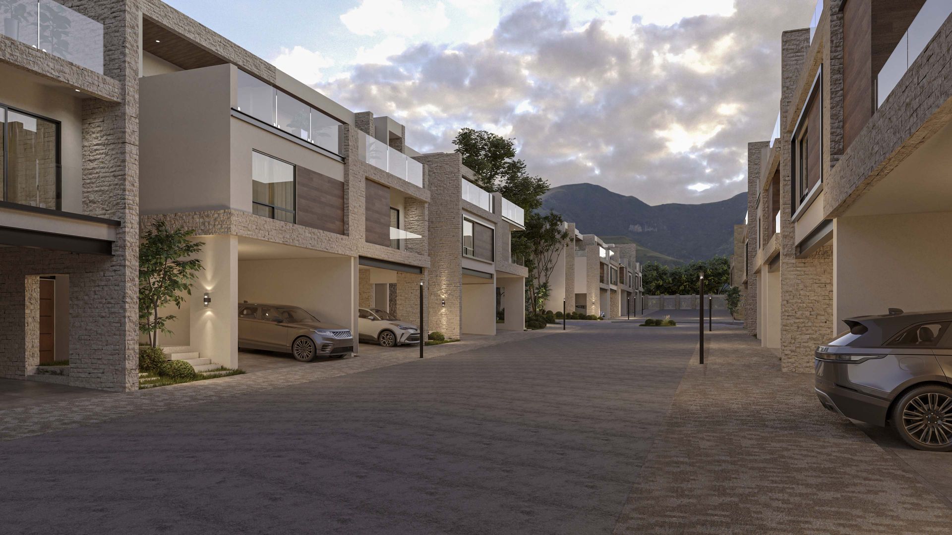 Patio de un moderno complejo de apartamentos con coches aparcados, edificios de piedra y montañas bajo un cielo nublado.