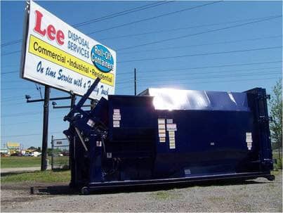 A dumpster is parked in front of a sign for lee disposal services