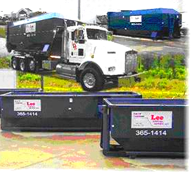 A dump truck is parked next to a dumpster on the side of the road.