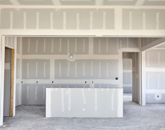 Interior of a building under construction, with drywall installed on walls and ceiling, grey and white.
