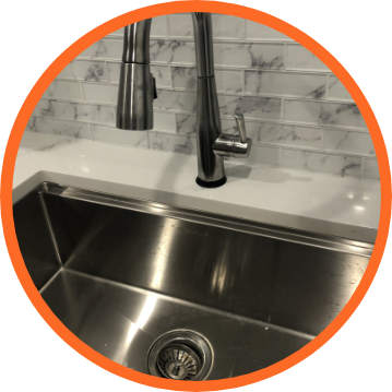 Stainless steel sink with faucet against white countertop and marble backsplash.