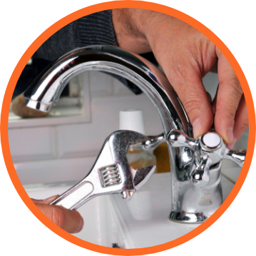 A person using an adjustable wrench on a chrome faucet in a bathroom.