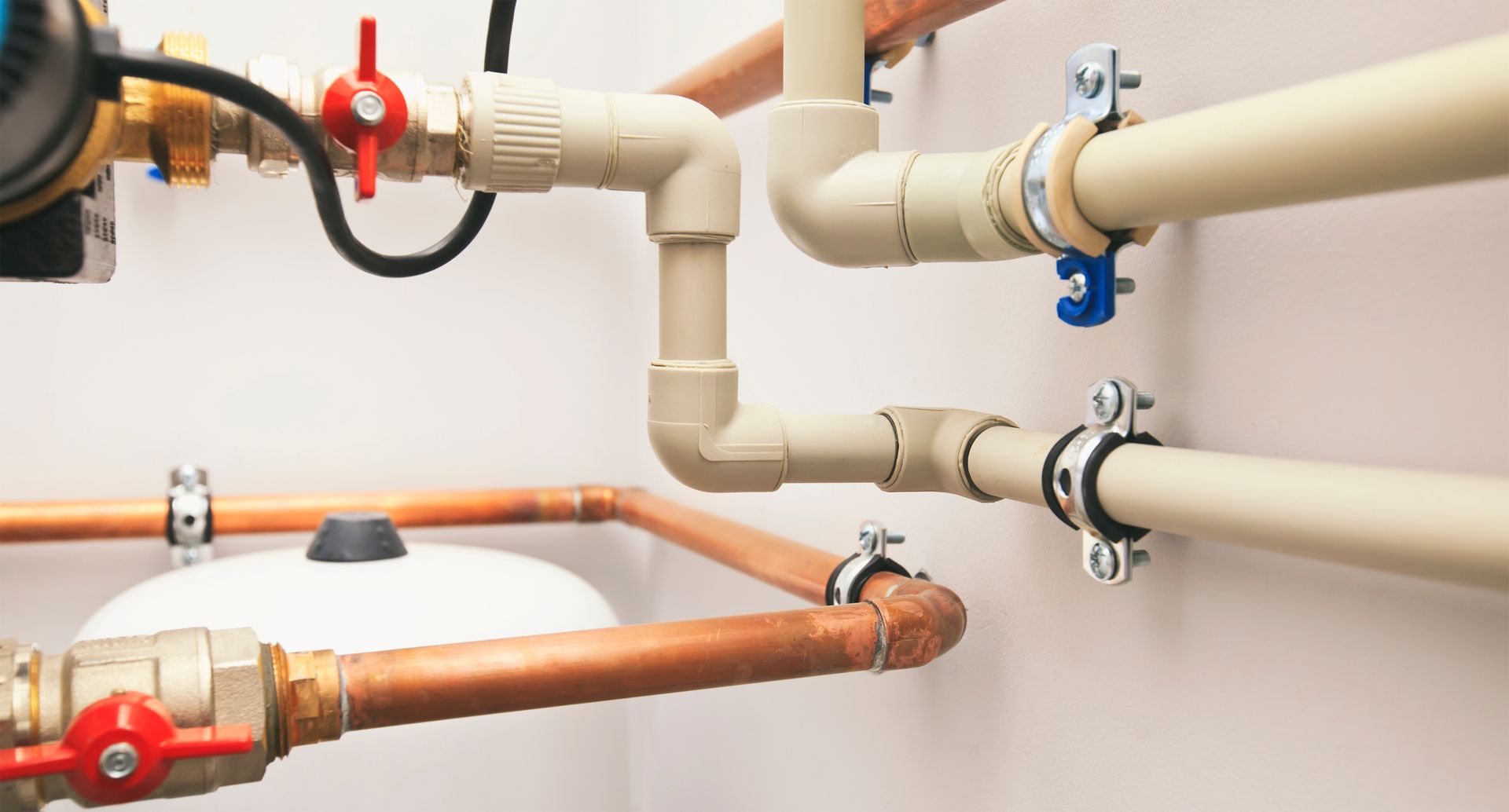 Different types of plumbing pipes connected in a boiler room.

