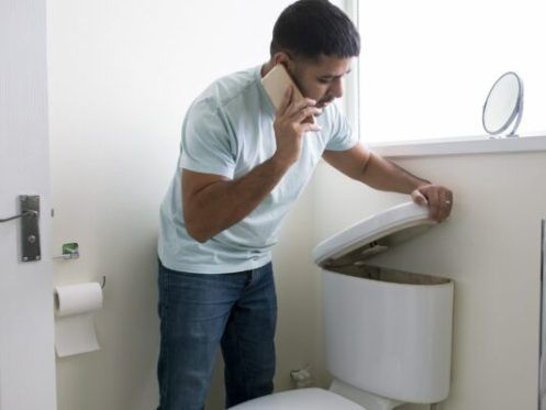 Man on phone looking at open toilet in bathroom.