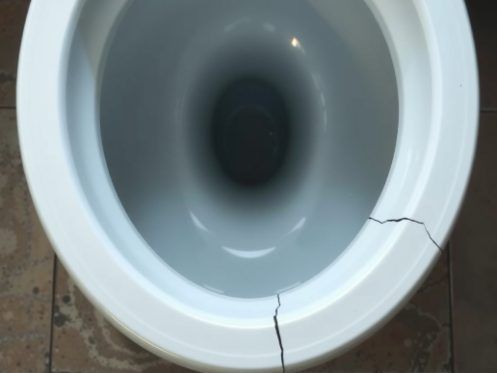 Cracked white toilet bowl. Tile floor visible around the base of the toilet.