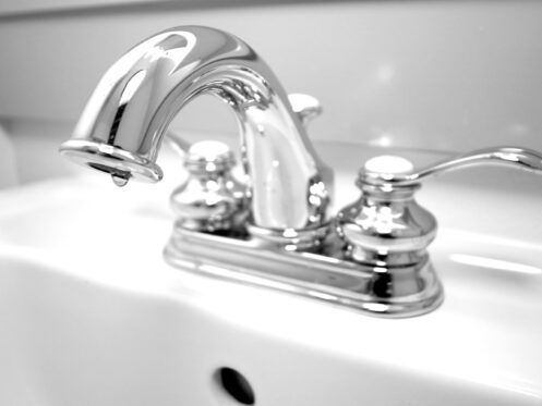 Shiny, silver faucet dripping water into a white sink.