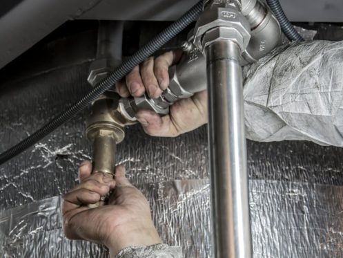 Hands of a plumber connecting metal pipes near insulation.