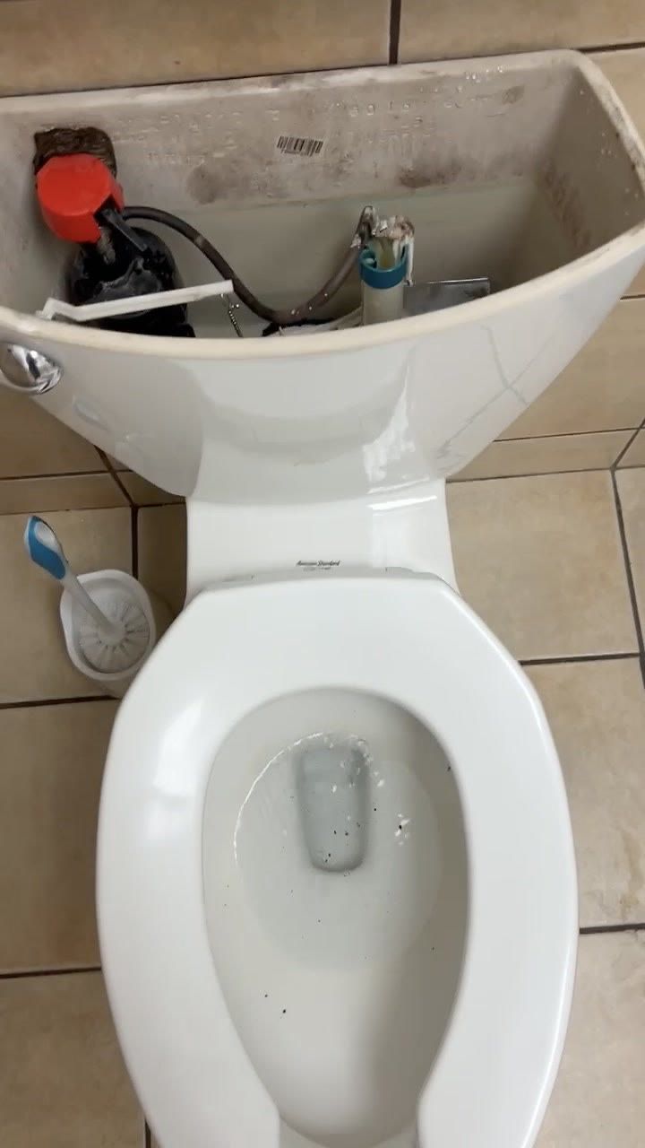 Open toilet tank showing the red fill valve cap, the refill hose, and the bowl below