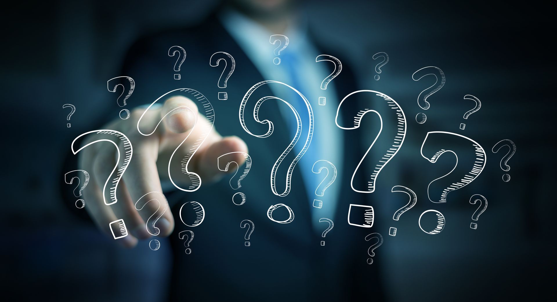A man in a suit is pointing at a bunch of question marks