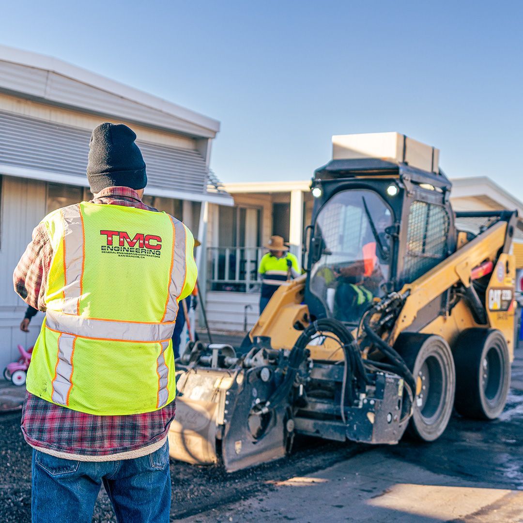 Workers in neon vests using a skid steer to clear a driveway beside a house