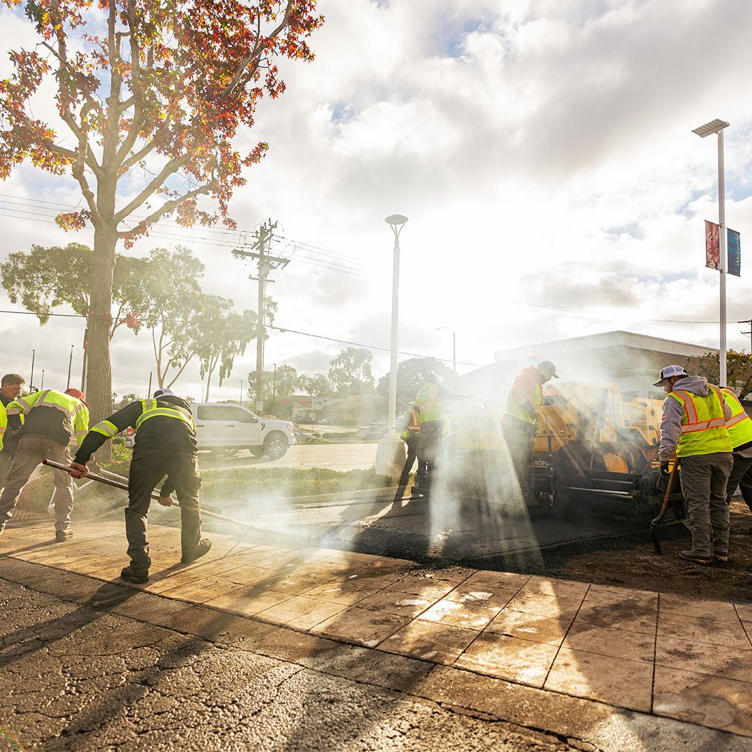 Firefighters douse a car blaze in a parking lot as sunlight and smoke fill the scene.
