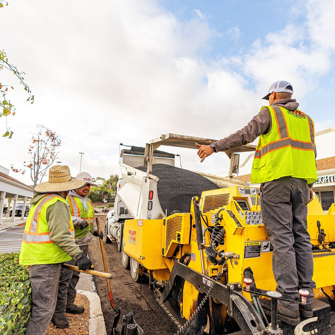 Construction workers operating a yellow paving machine under cloudy skies