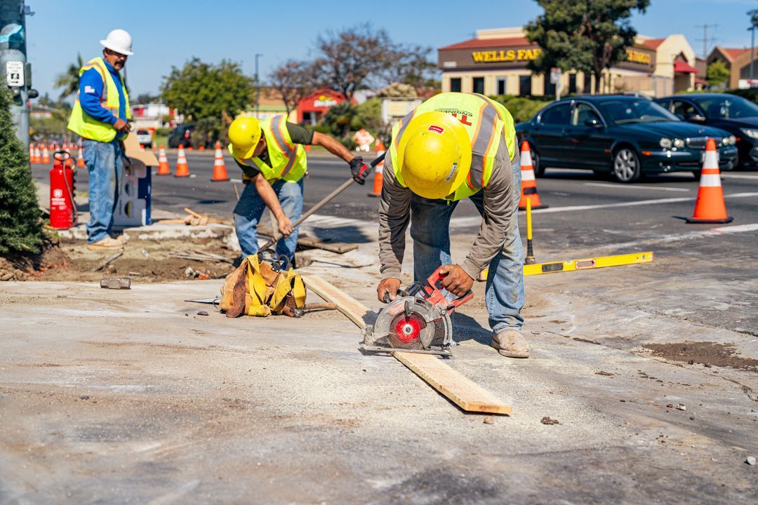 A group of construction workers are working on a sidewalk in a parking lot.