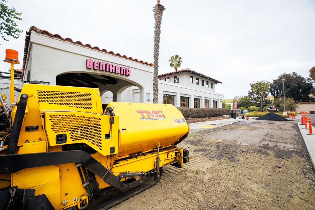 Yellow road paving machine on a street beside a white building under construction