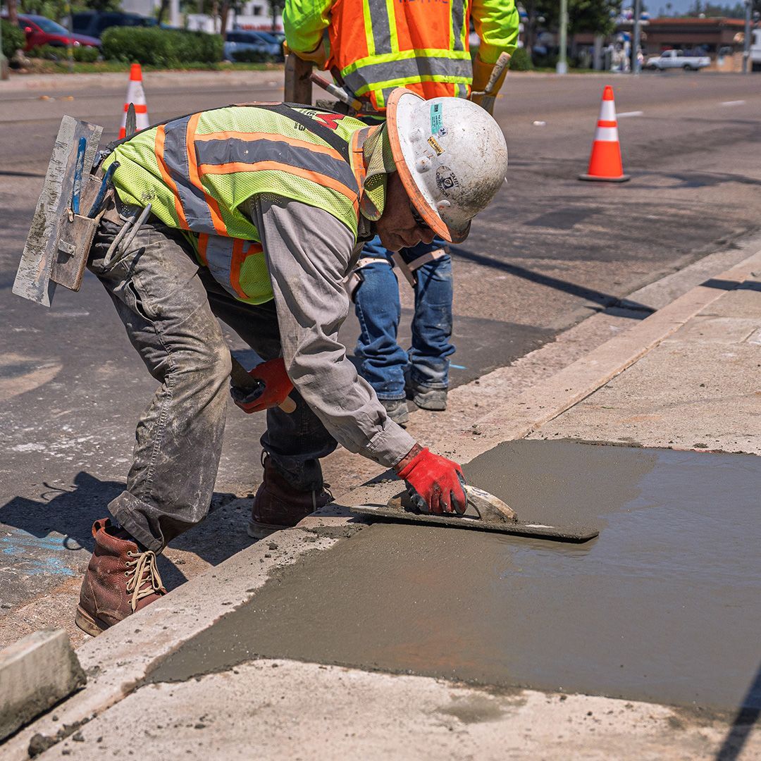Road workers smoothing fresh concrete near orange traffic cones on a street repair site