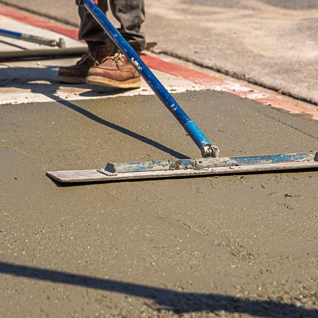 Worker leveling fresh concrete with a blue screed on a driveway site