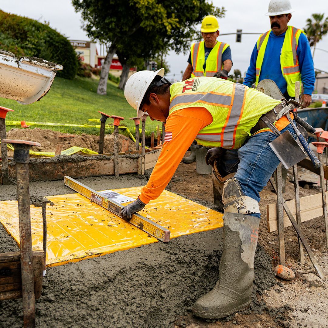 Construction workers pouring concrete at a site, with one smoothing a yellow formwork slab.