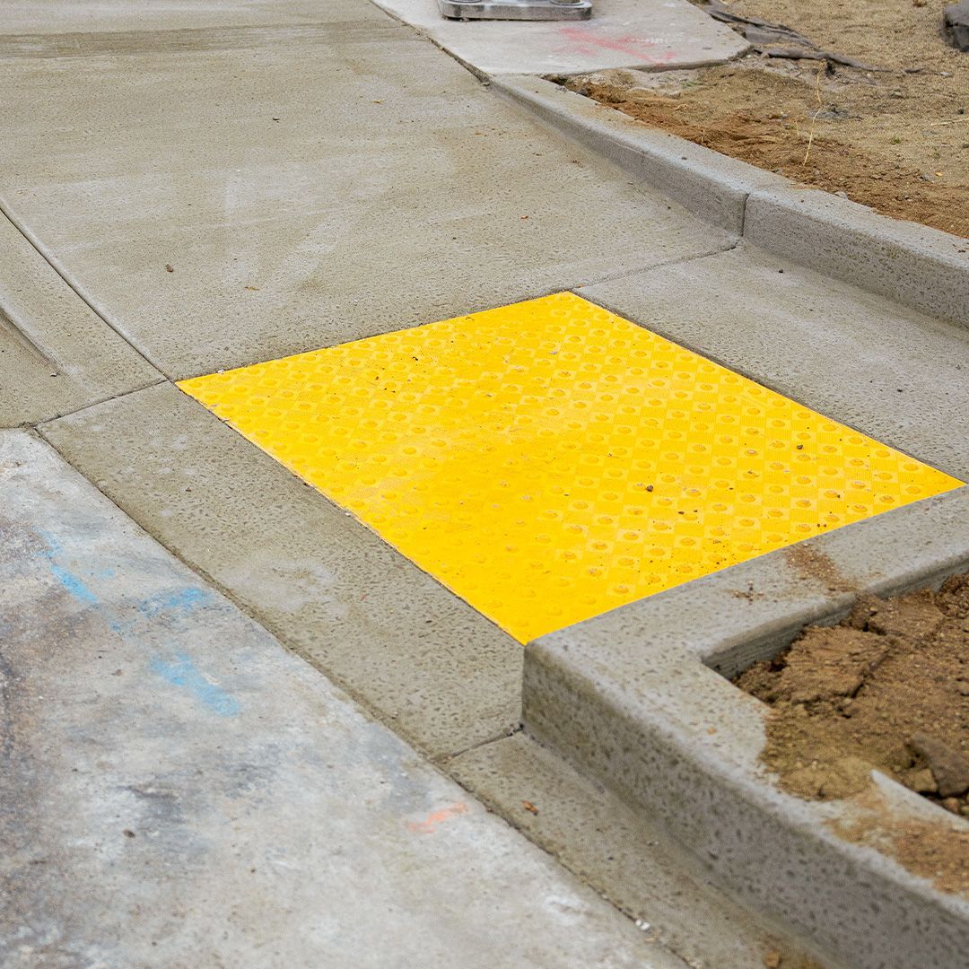 Bright yellow tactile paving panel at a curb cut beside a concrete sidewalk