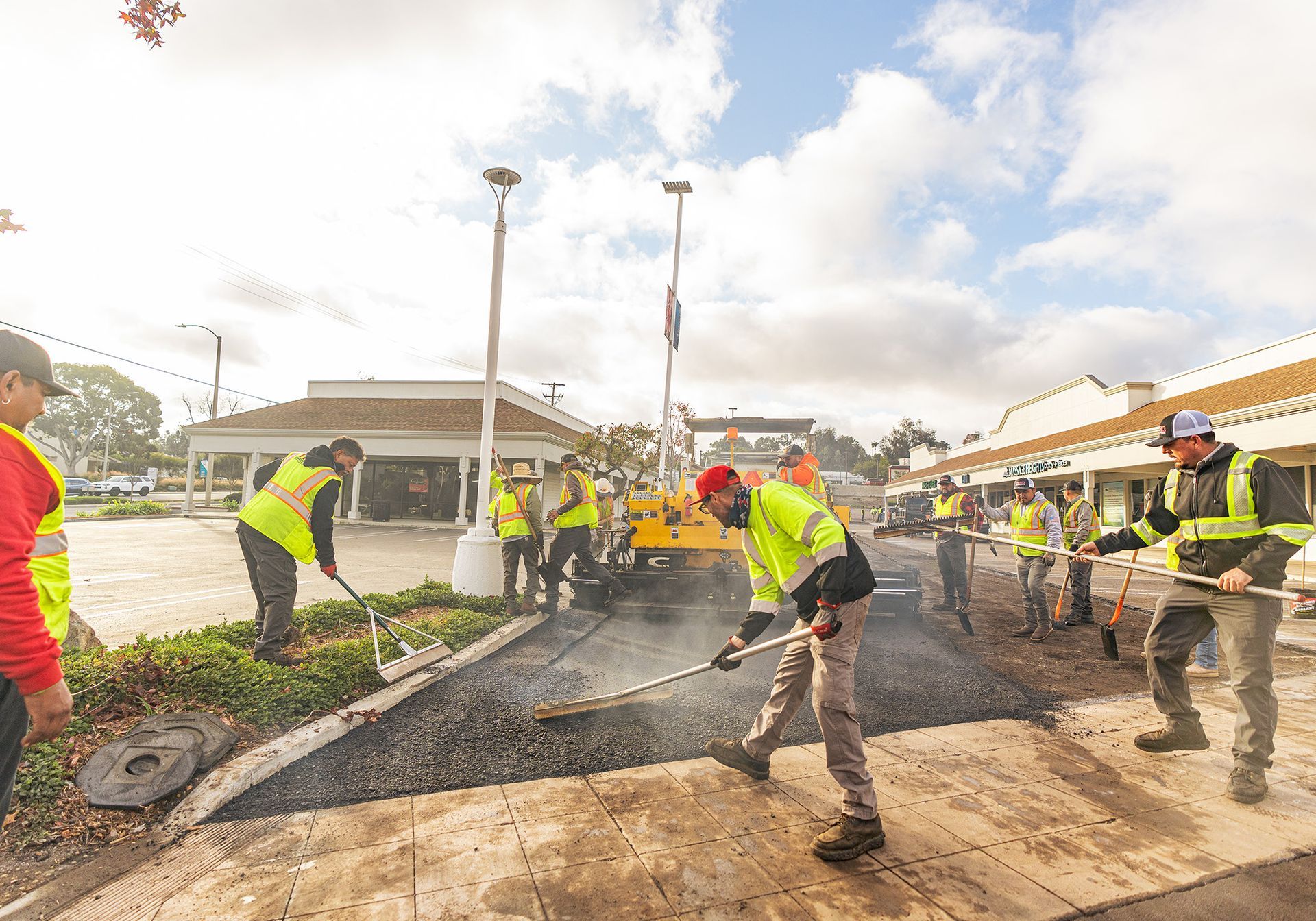 Workers in yellow safety vests paving a road with shovels at a construction site.