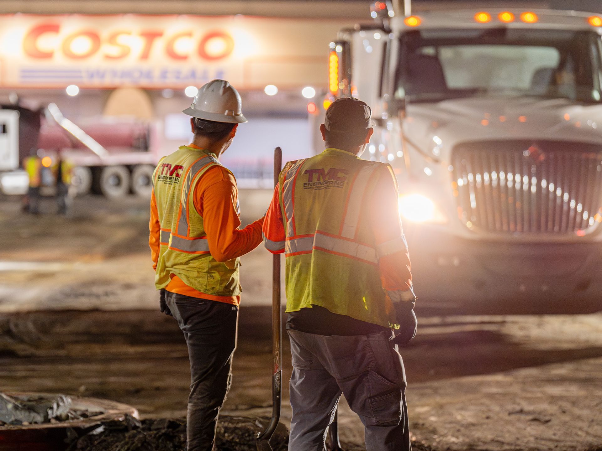 Two construction workers are standing in front of a costco truck.