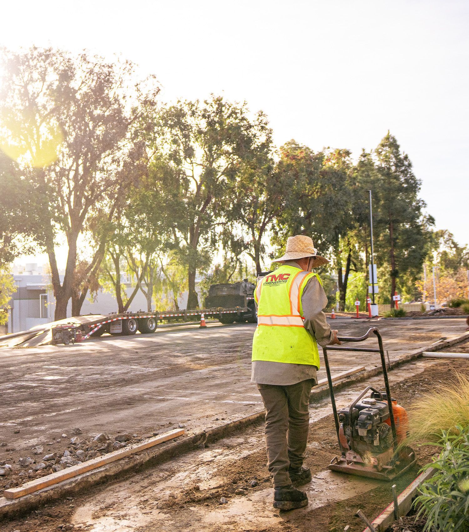 A man in a yellow vest and hat is standing on a dirt road.