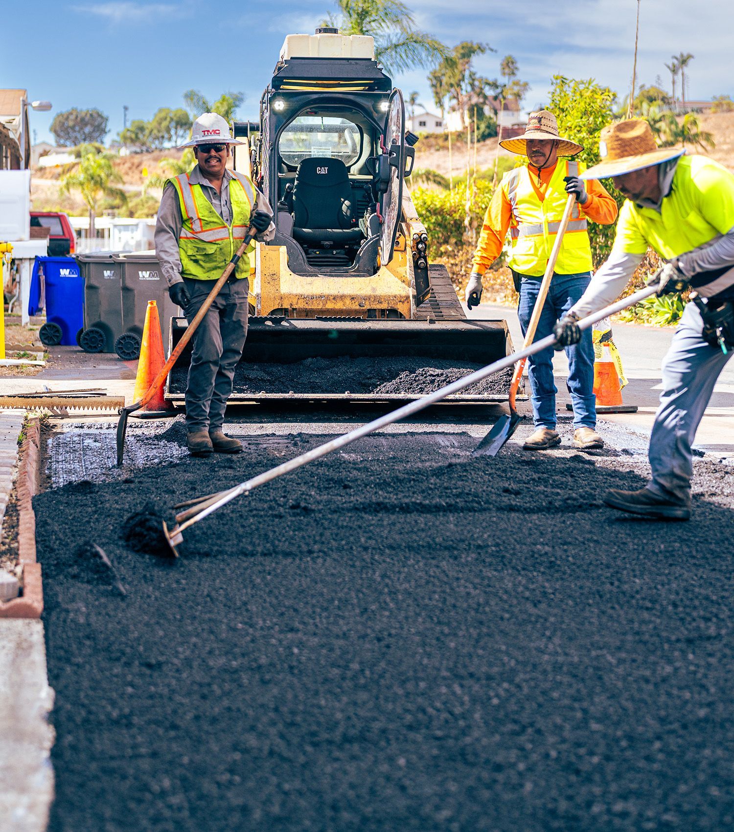 Road crew paving asphalt with rakes and a road roller in the background