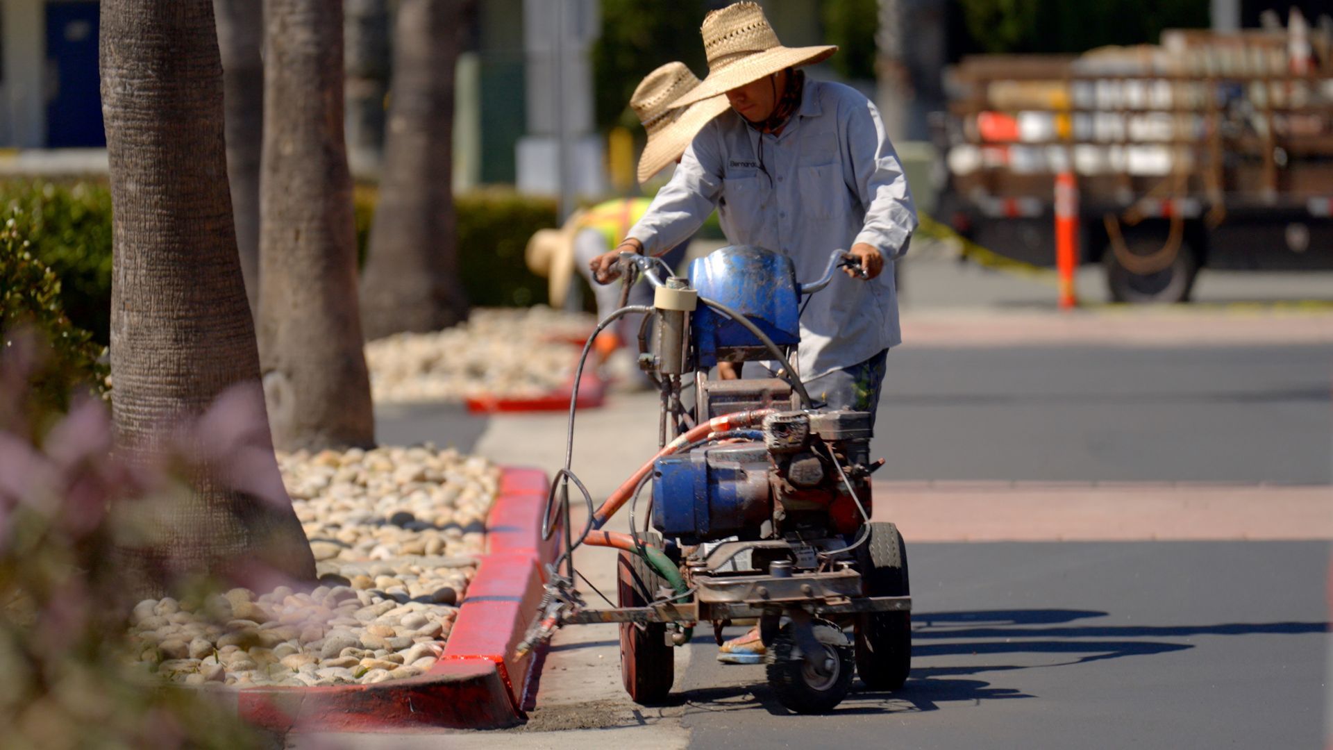 A man is using a machine to paint a curb on the side of the road.