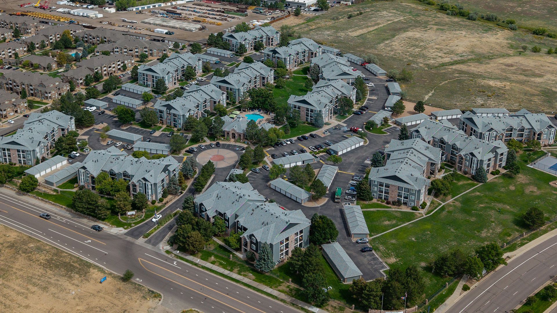 Aerial view of a suburban apartment complex with gray rooftops, roads, and surrounding green lawns.