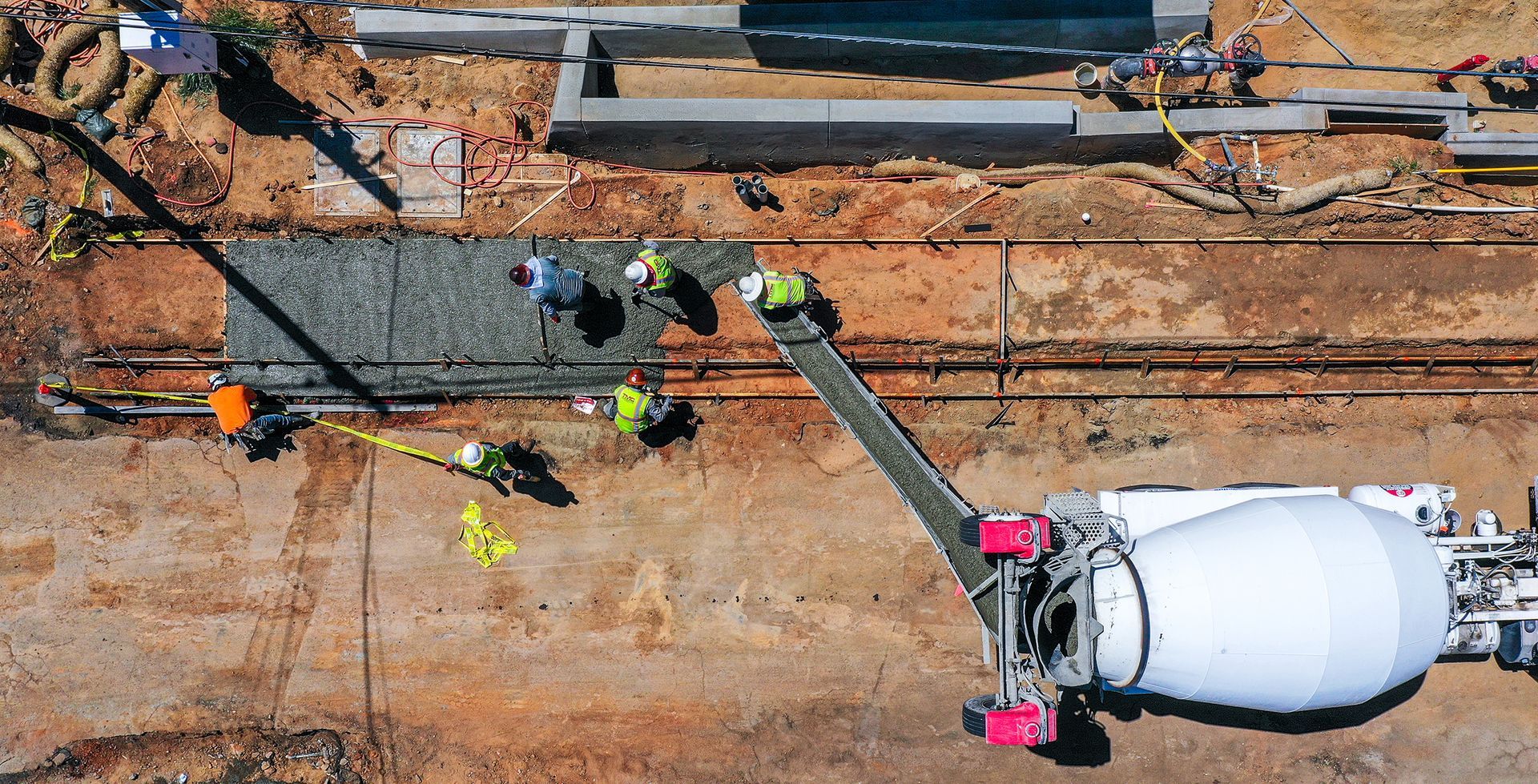 Construction workers paving a road beside a white cement mixer truck at a worksite