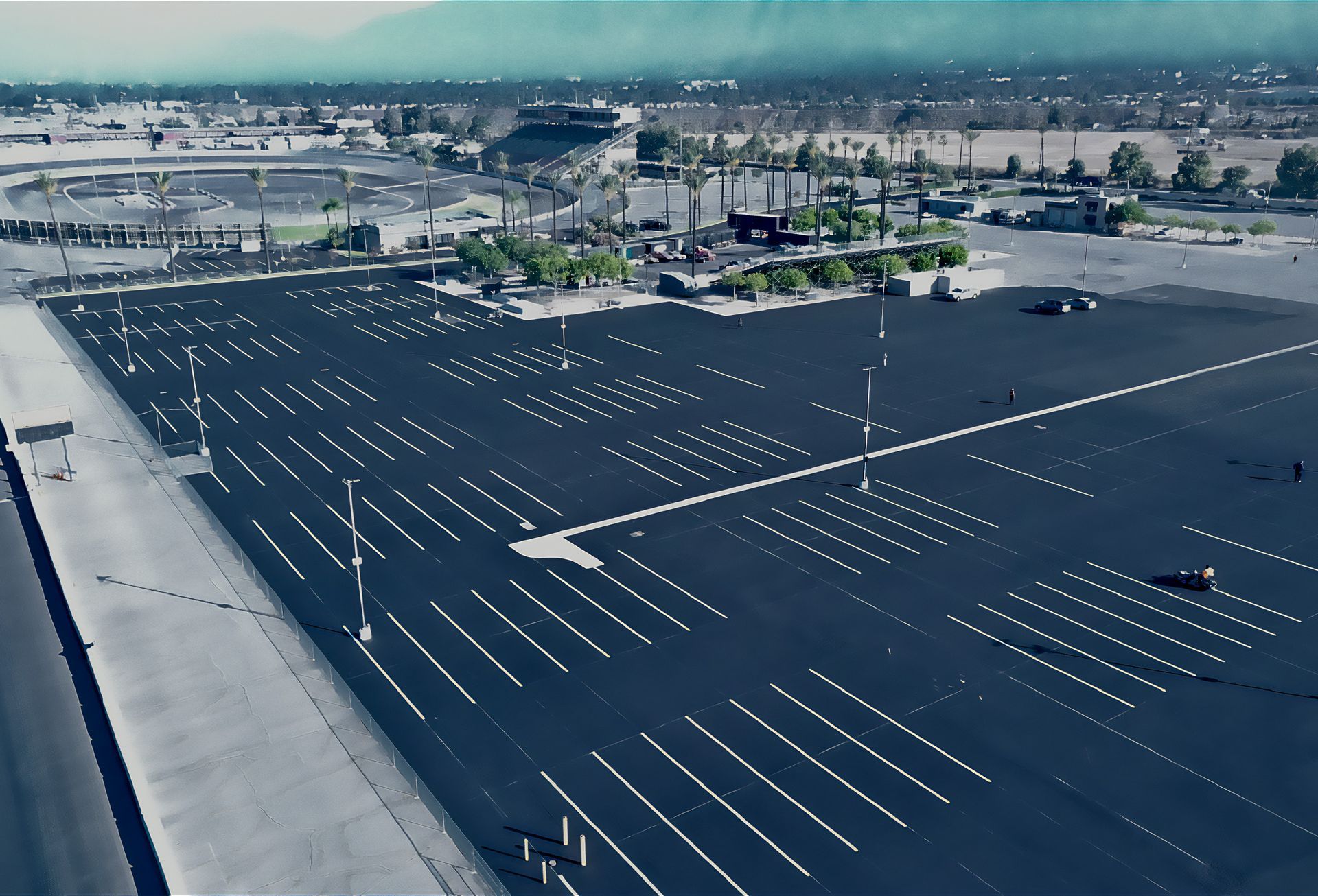 An aerial view of an empty parking lot with palm trees in the background