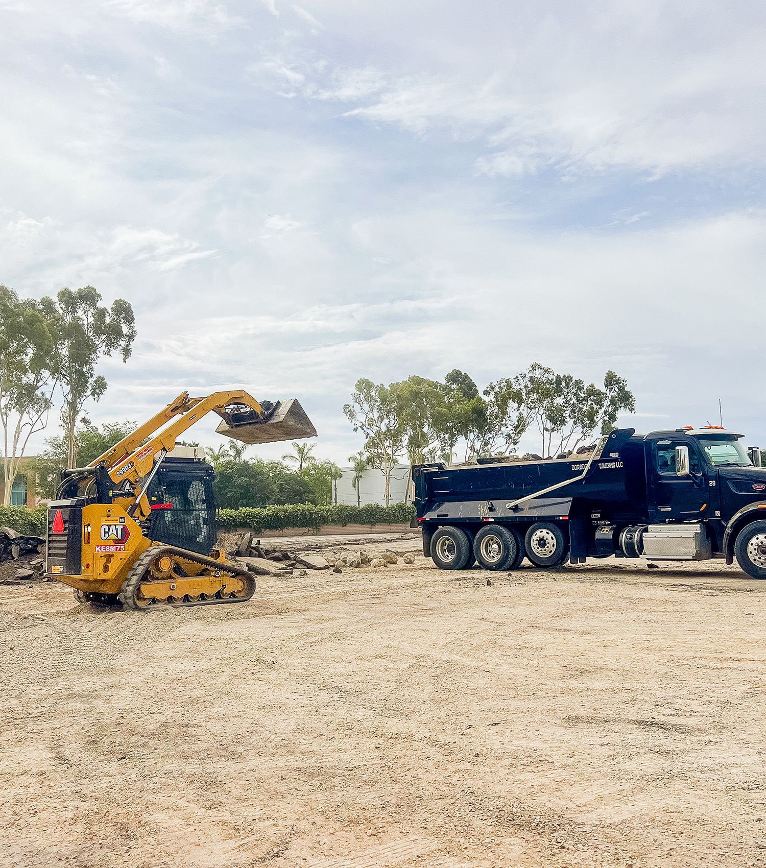 A dump truck is being towed by a bulldozer in a dirt field.