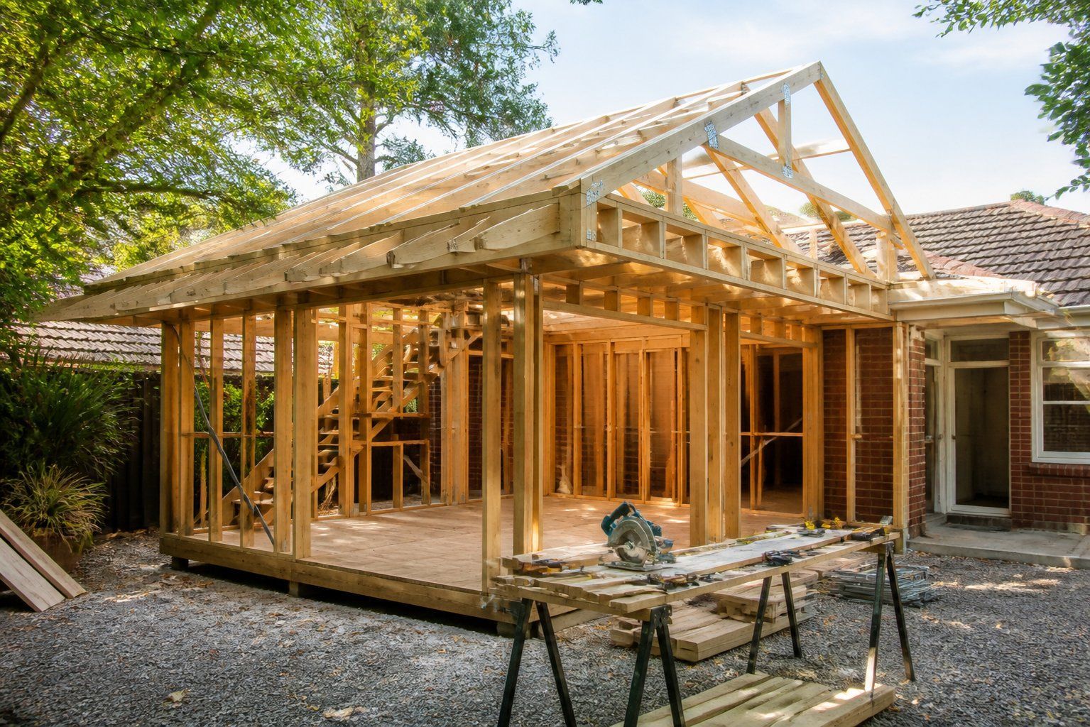 Partially built wooden house frame under construction beside an existing brick home