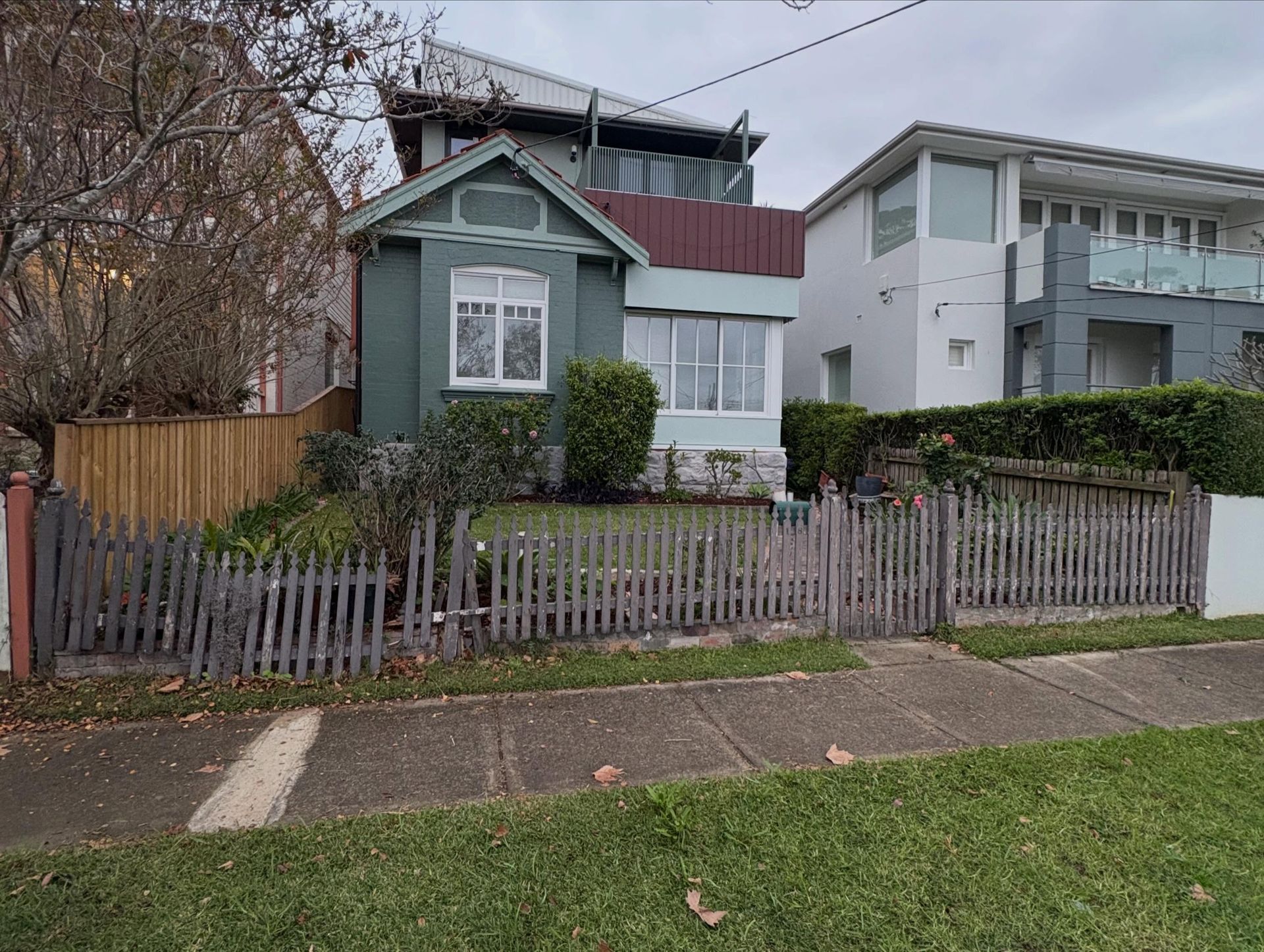 Small green house with a fenced front yard and sidewalk in a residential neighborhood