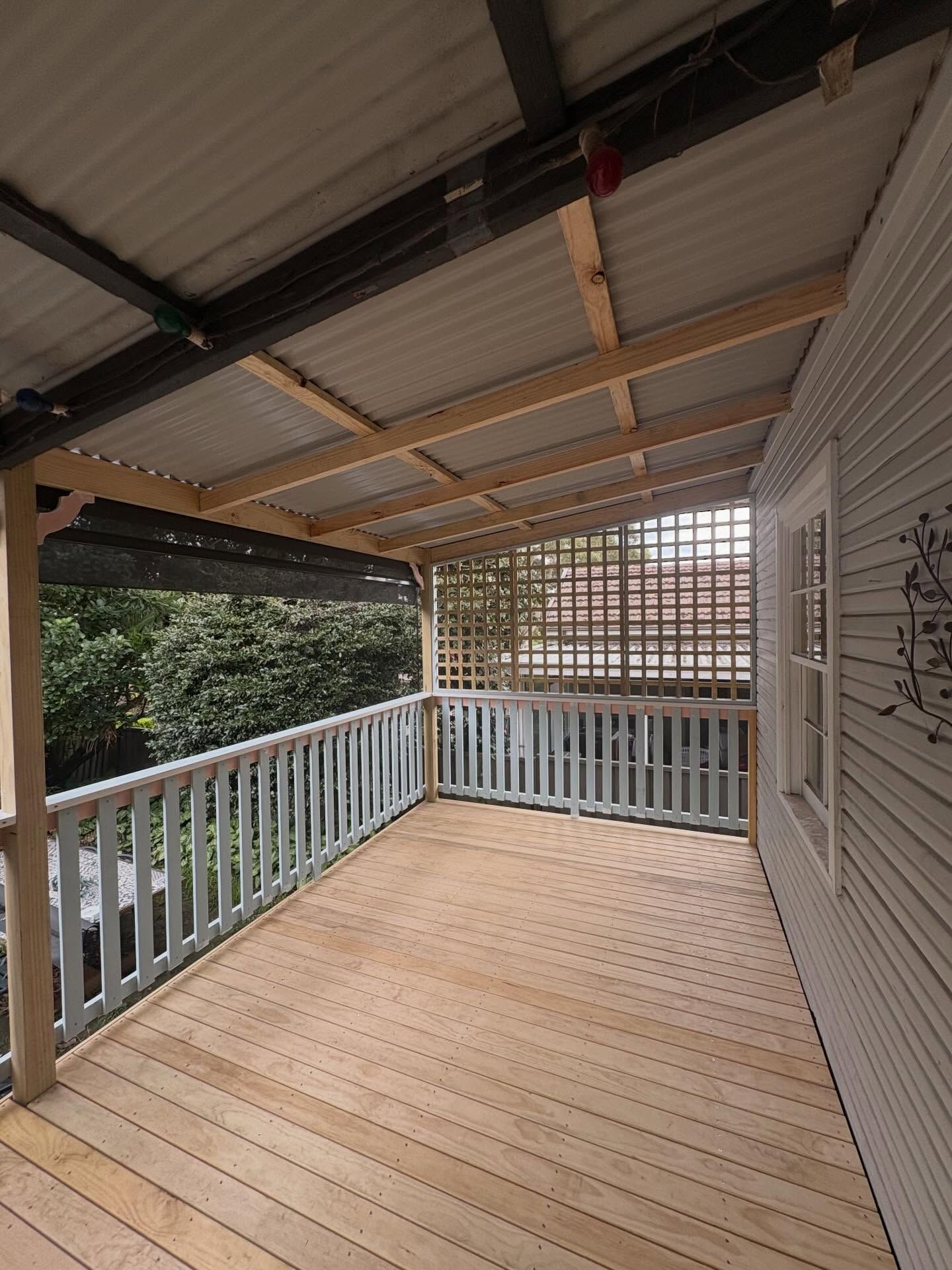 Wooden covered porch with white railings and lattice wall, overlooking trees.