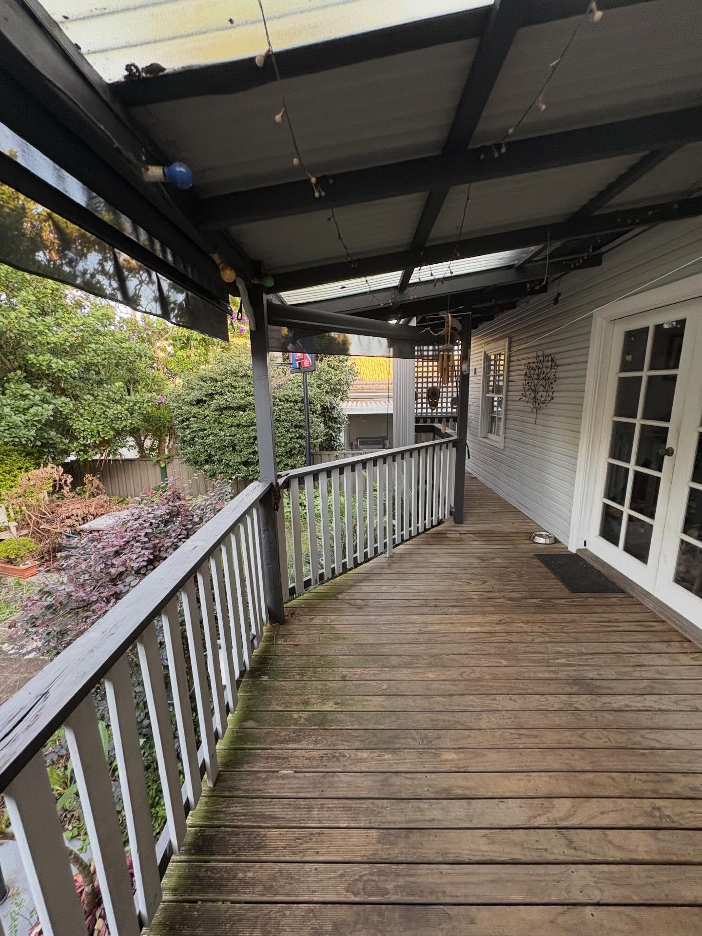 Covered wooden porch with white railing and French doors beside a garden