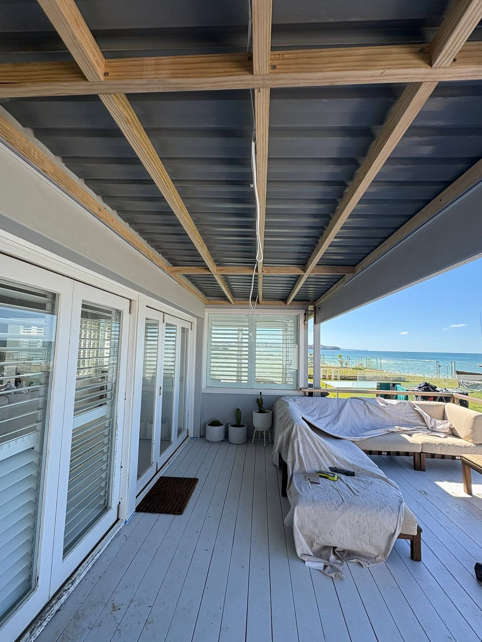 Covered seaside patio with lounge chairs, dining table, and ocean view beyond railing
