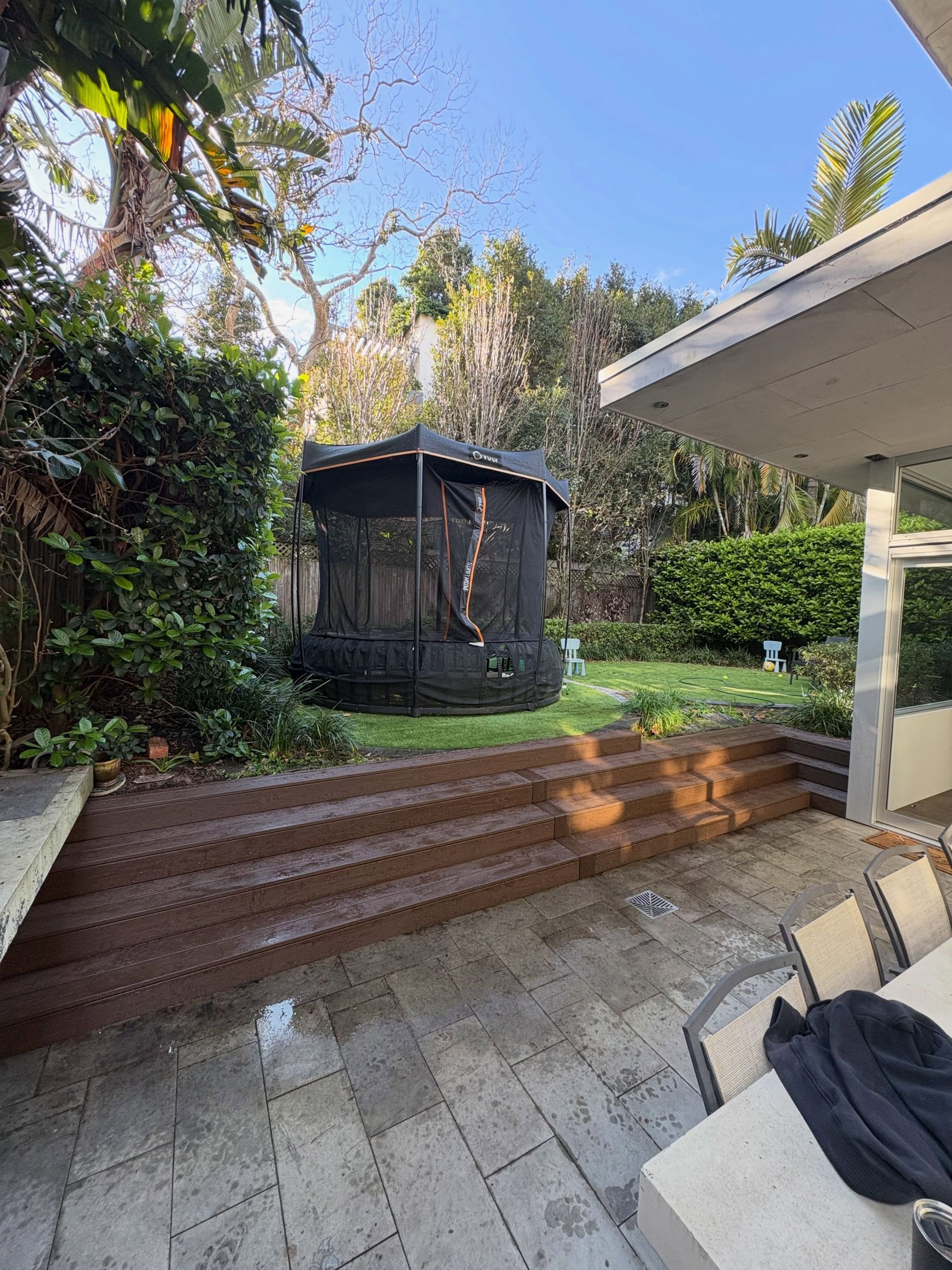 Backyard patio with a black mesh gazebo, brick steps, and green landscaping under a blue sky