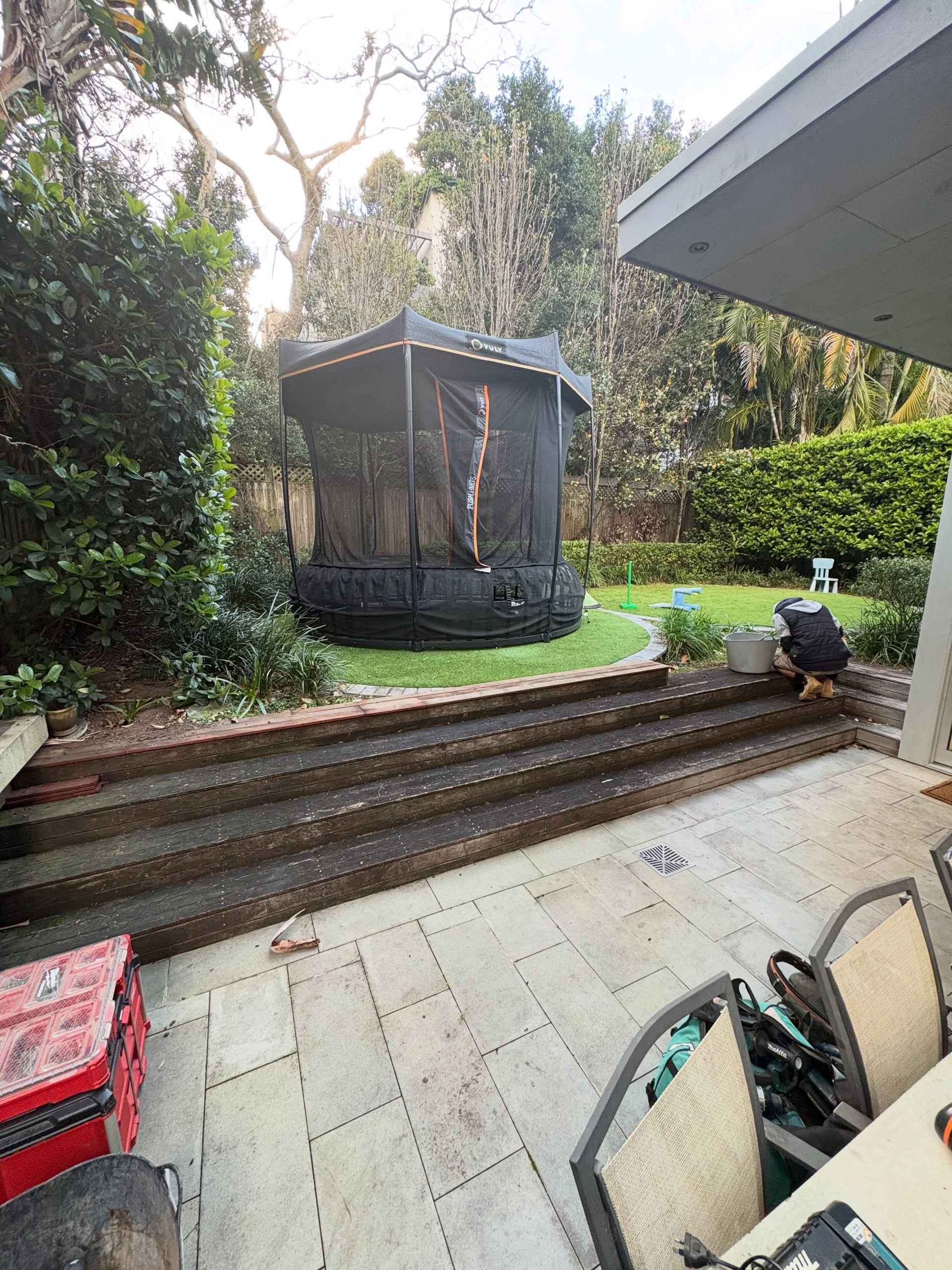 Backyard patio with steps to a grassy yard, a screened gazebo, and outdoor chairs in the foreground