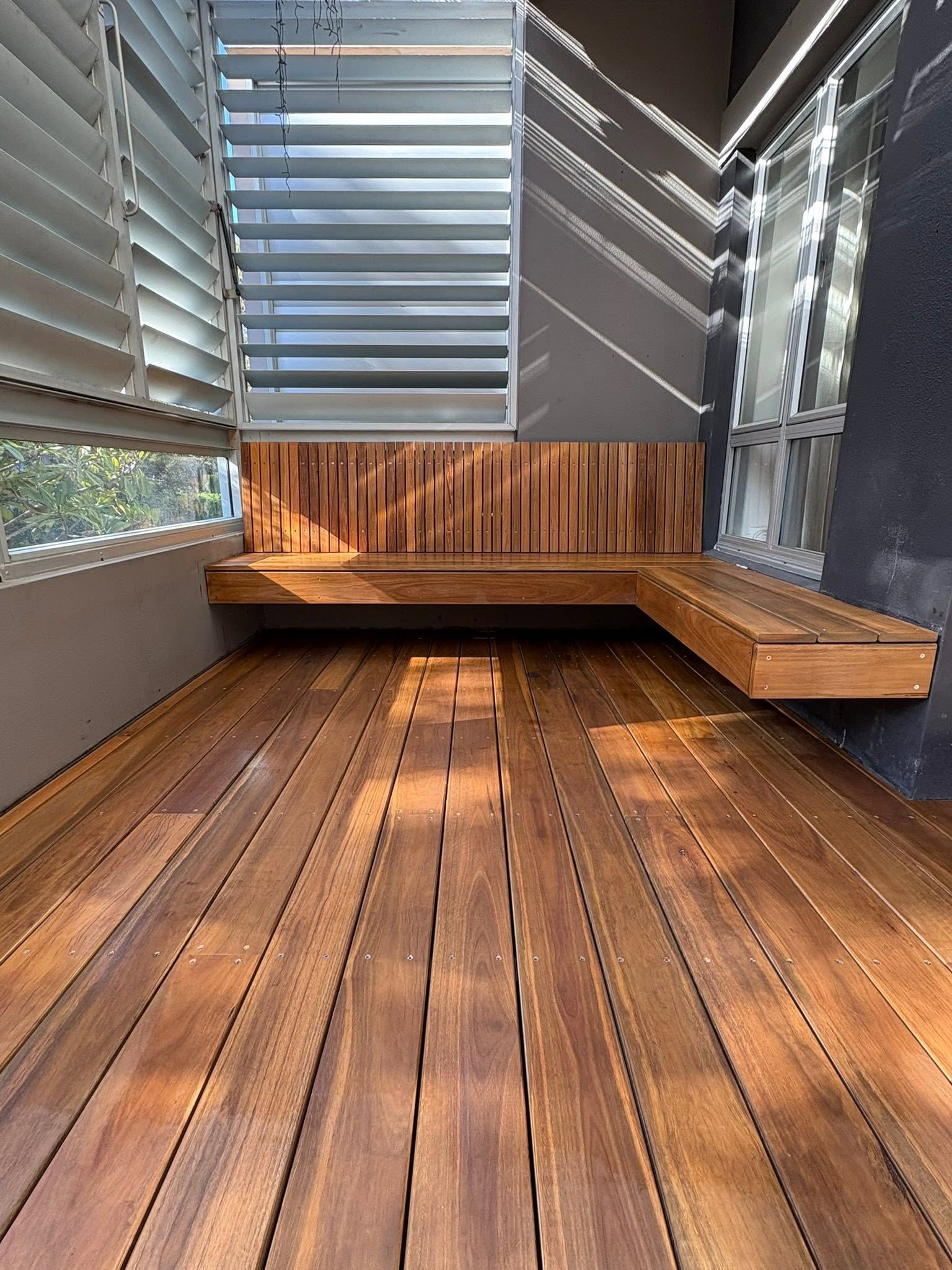 Modern outdoor wooden deck with louvered windows and built-in bench seating in a shaded corner