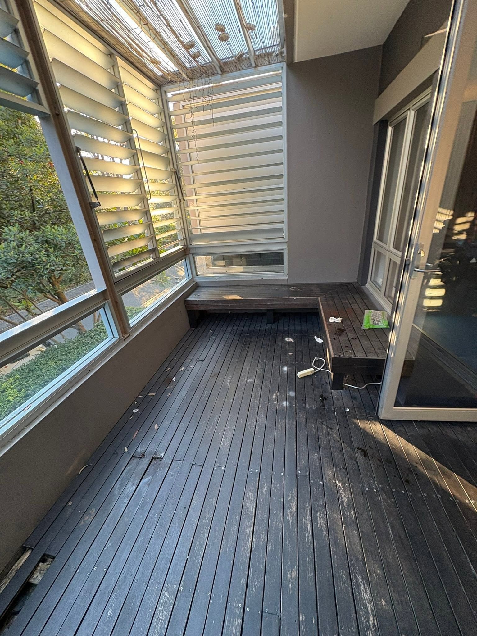 Sunlit screened porch with dark flooring, gray bench seating, and metal slatted wall panels