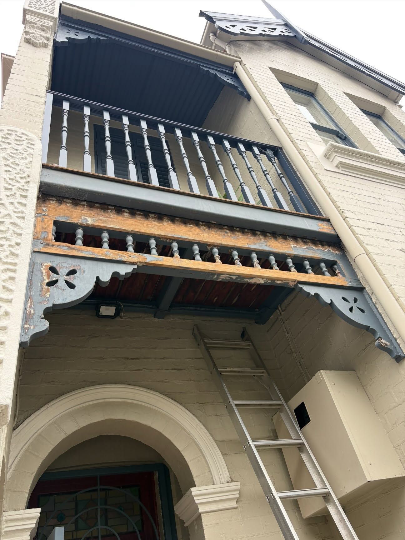 Balcony of a brick townhouse with a ladder leaning against the entrance below